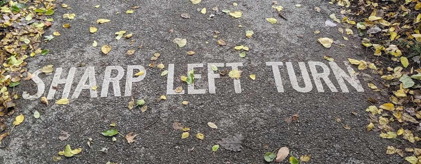 Sharp left turn written in white on a walking path