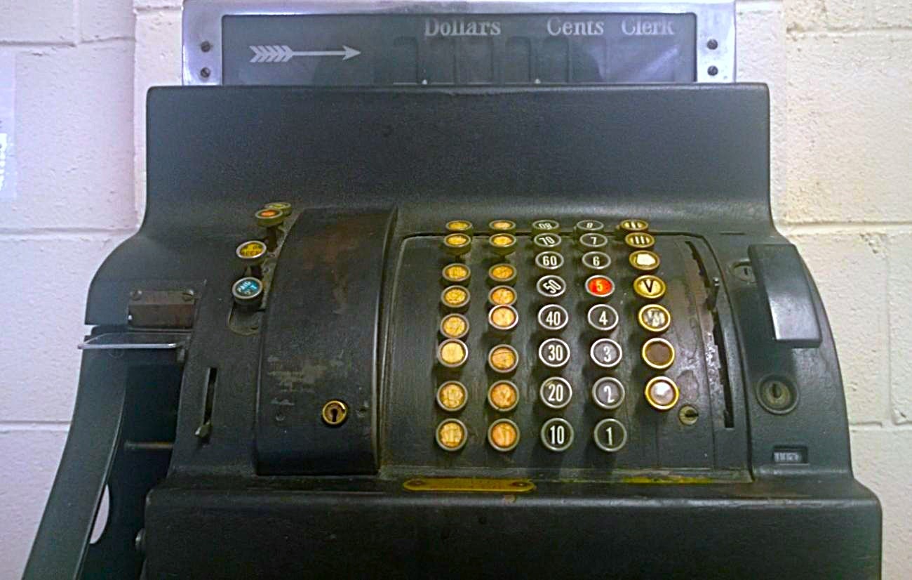 A vintage mechanical cash register with round, color-coded buttons arranged in vertical columns, each labeled with numbers or symbols like 