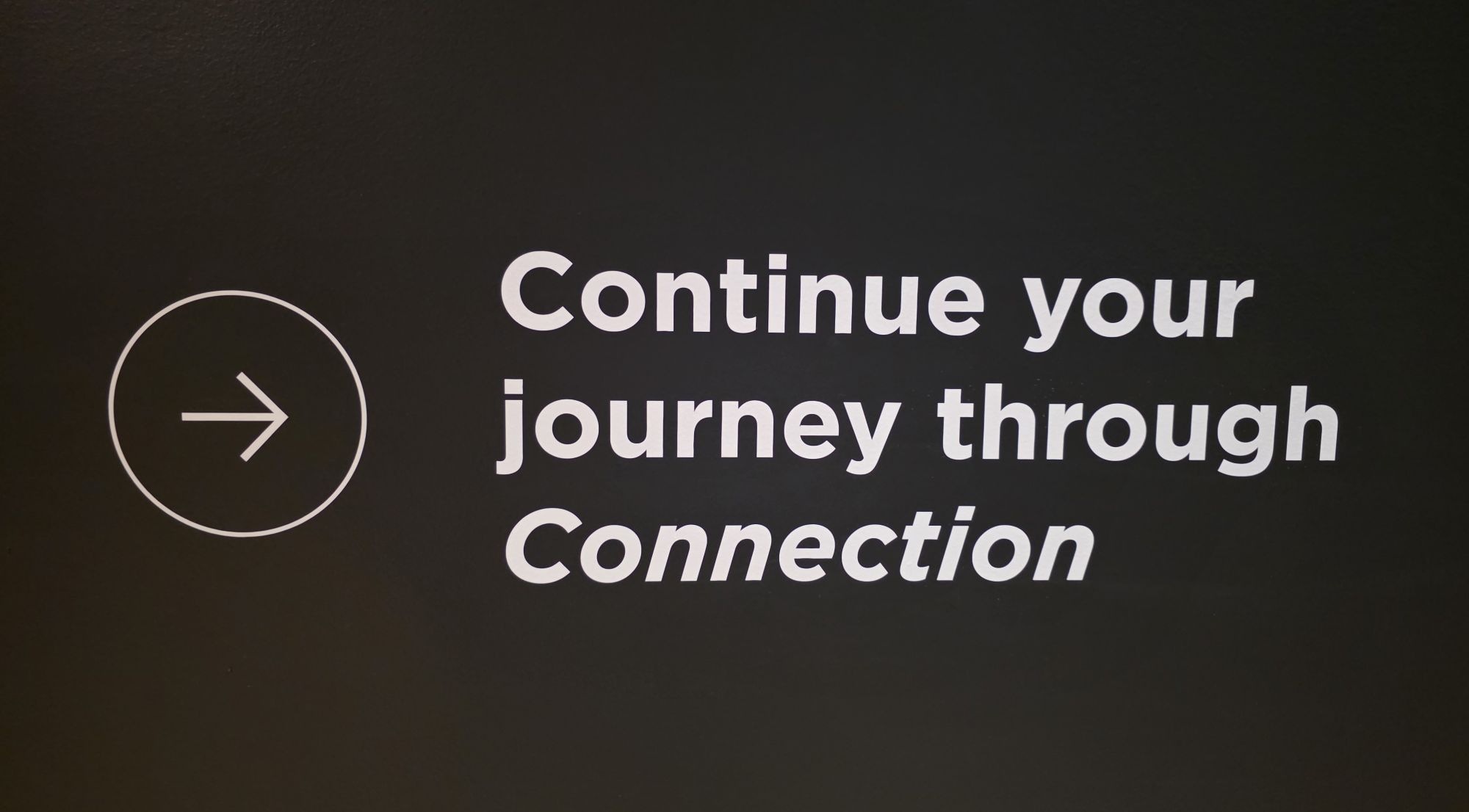 Text includes the words Continue your journey through Connection. With the Connection italicized for emphasis. Suggests forward movement and thematic focus on connection, from within a curated exhibit in Indianapolis.