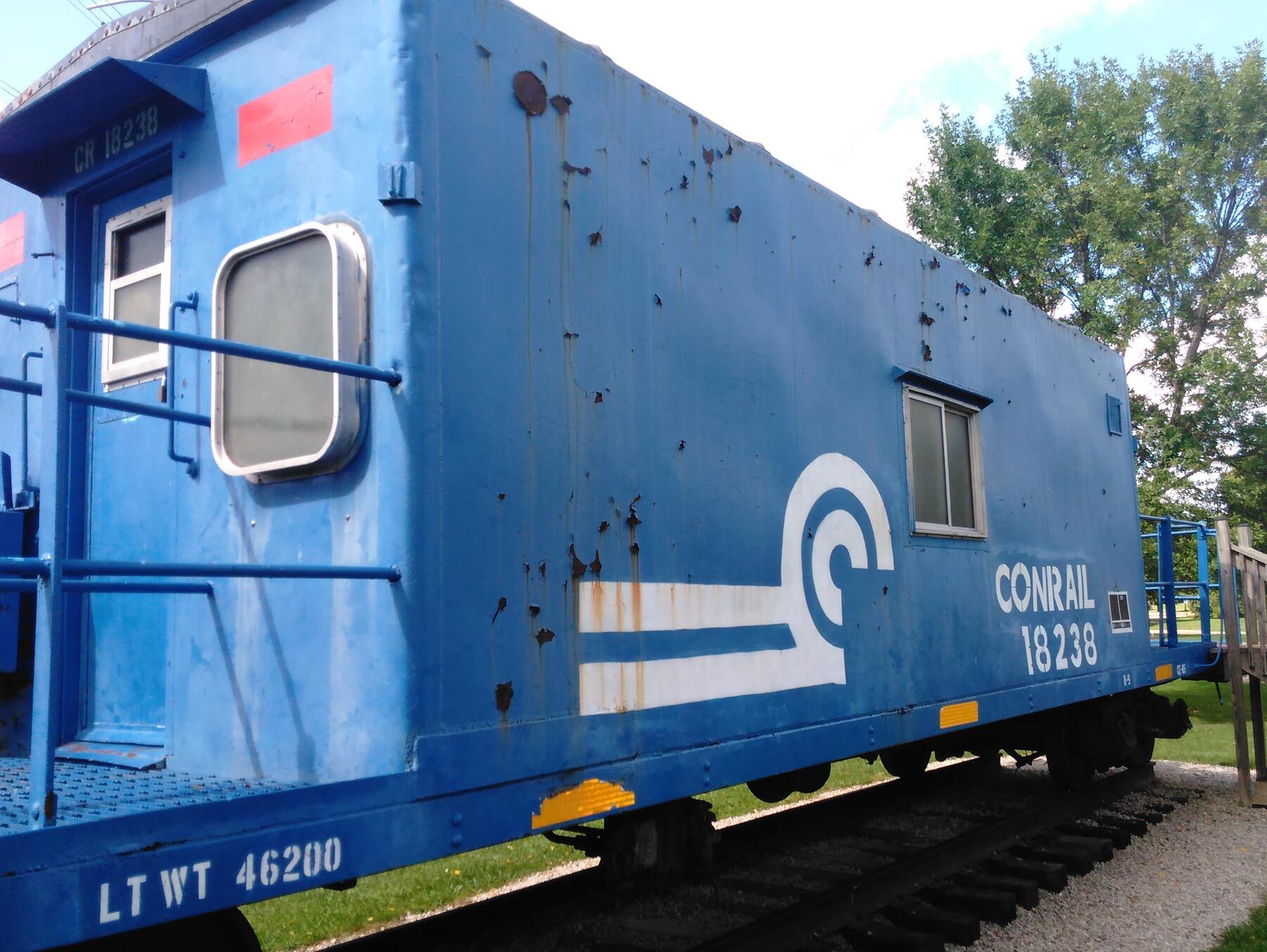 A weathered Conrail caboose, number 18238, painted in faded blue with rust patches across the side panel and the white Conrail wheel-of-fortune logo still visible above the reporting marks.