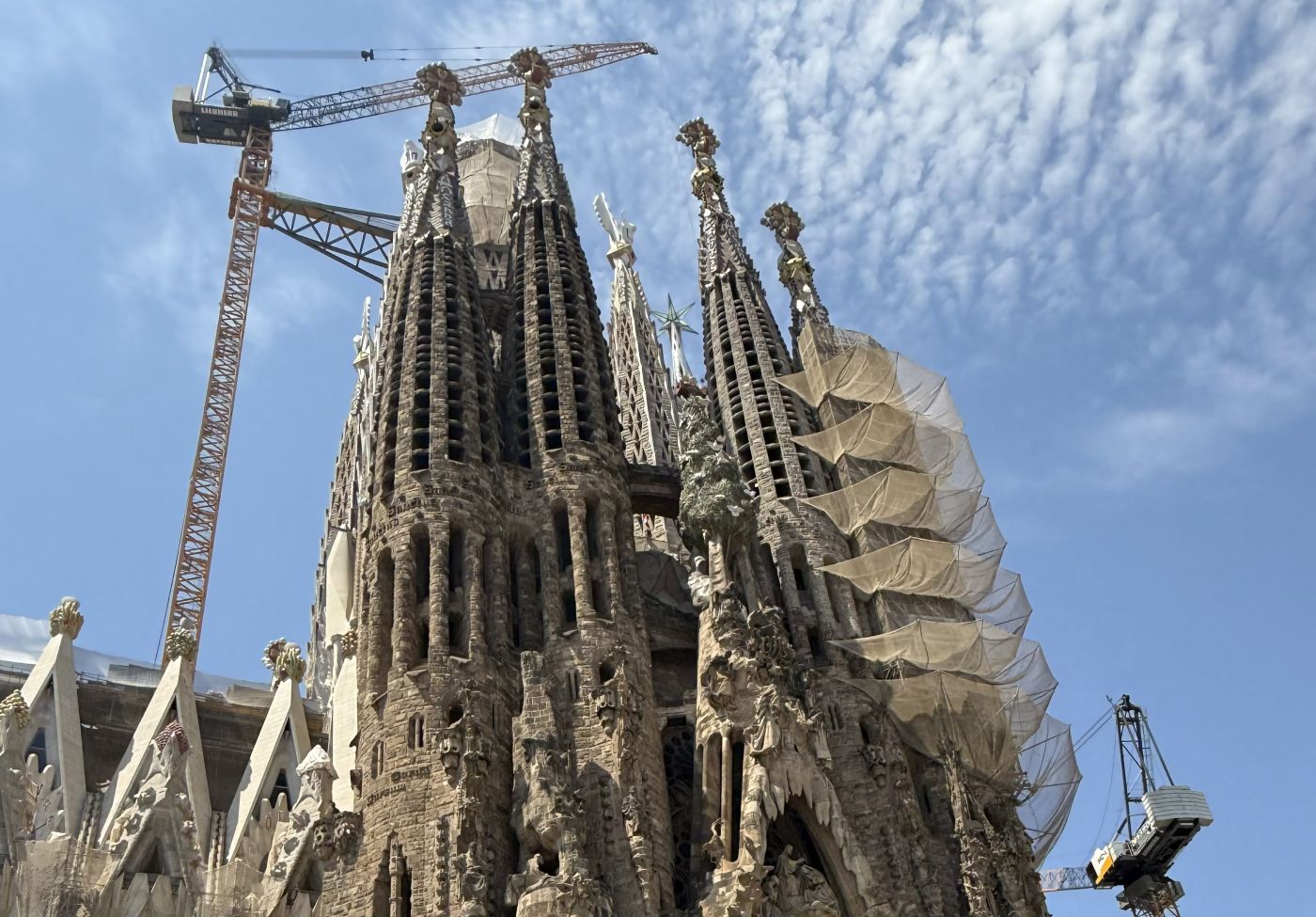 Construction cranes and scaffolding netting surround the ornate stone towers of Gaudí's Sagrada Familia in Barcelona, a basilica begun in 1882 and still under construction.